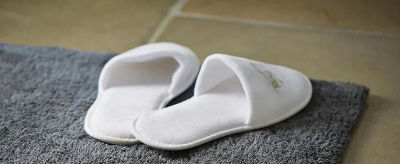 Soft cream bamboo bath mat in a shower room with a plant and some shampoo sitting on the floor and a bale of towels in the background