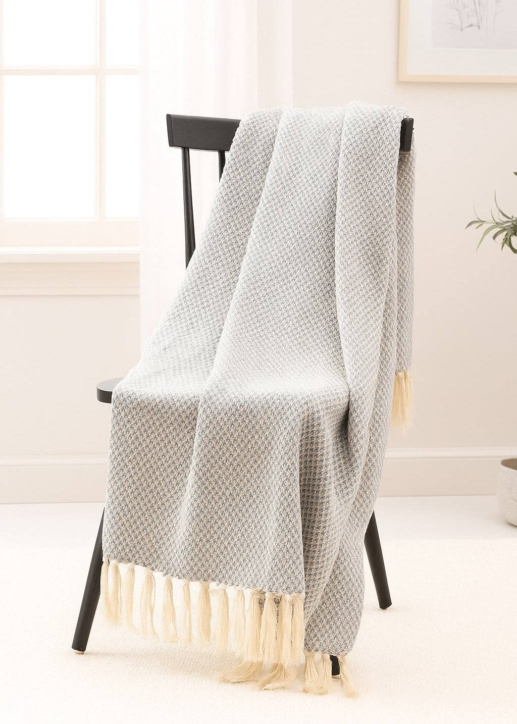 Blue textured throw blanket with fringes draped over a chair in a room with a light background.
