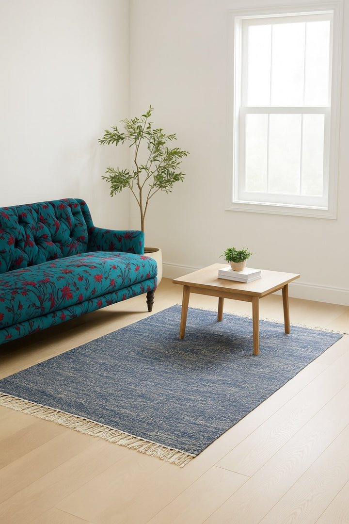 Blue cotton rug with fringe in modern living room, styled with wood table, plant, and teal floral sofa