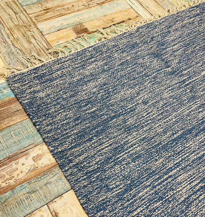 Close Up of Blue Drift Heavy Cotton Rug with a fringe on a wooden floor.