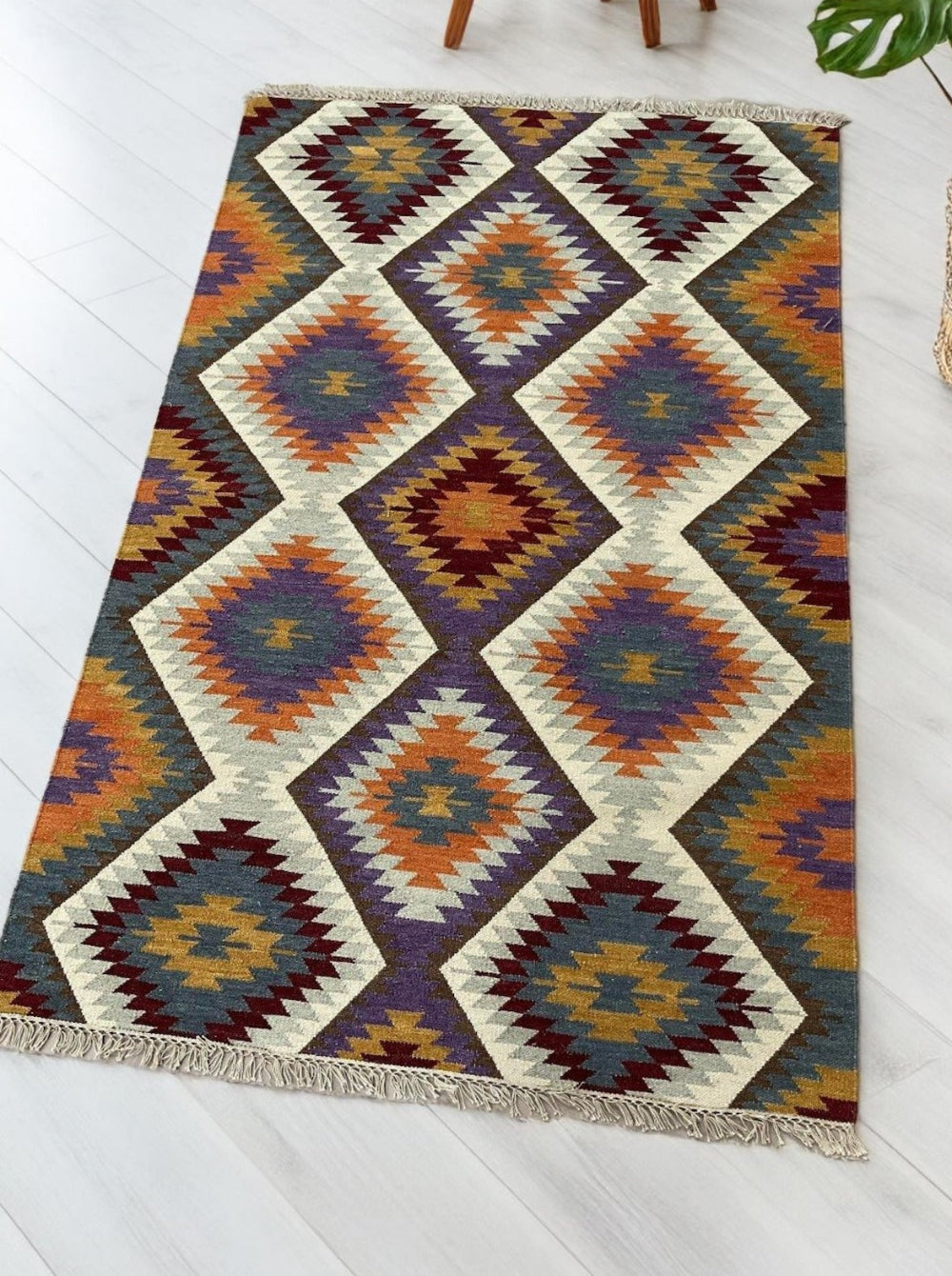 Flatweave kilim rug with multicolour diamond pattern in orange, blue, burgundy and cream tones on light wood flooring.