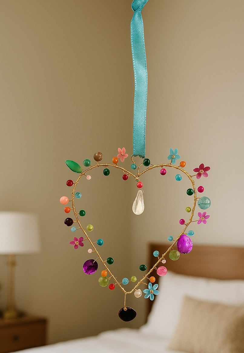 Decorative heart-shaped hanging ornament with colourful beads and flowers on a neutral background