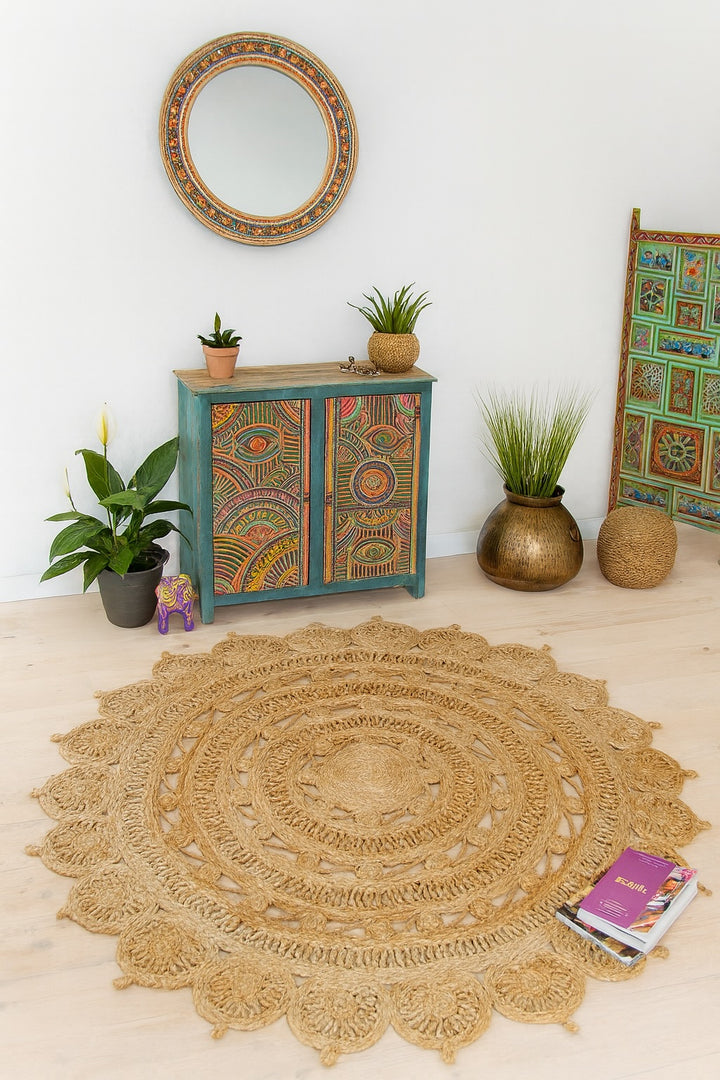 Round jute rug on a light wooden floor with decorative cabinet and plants in a room.