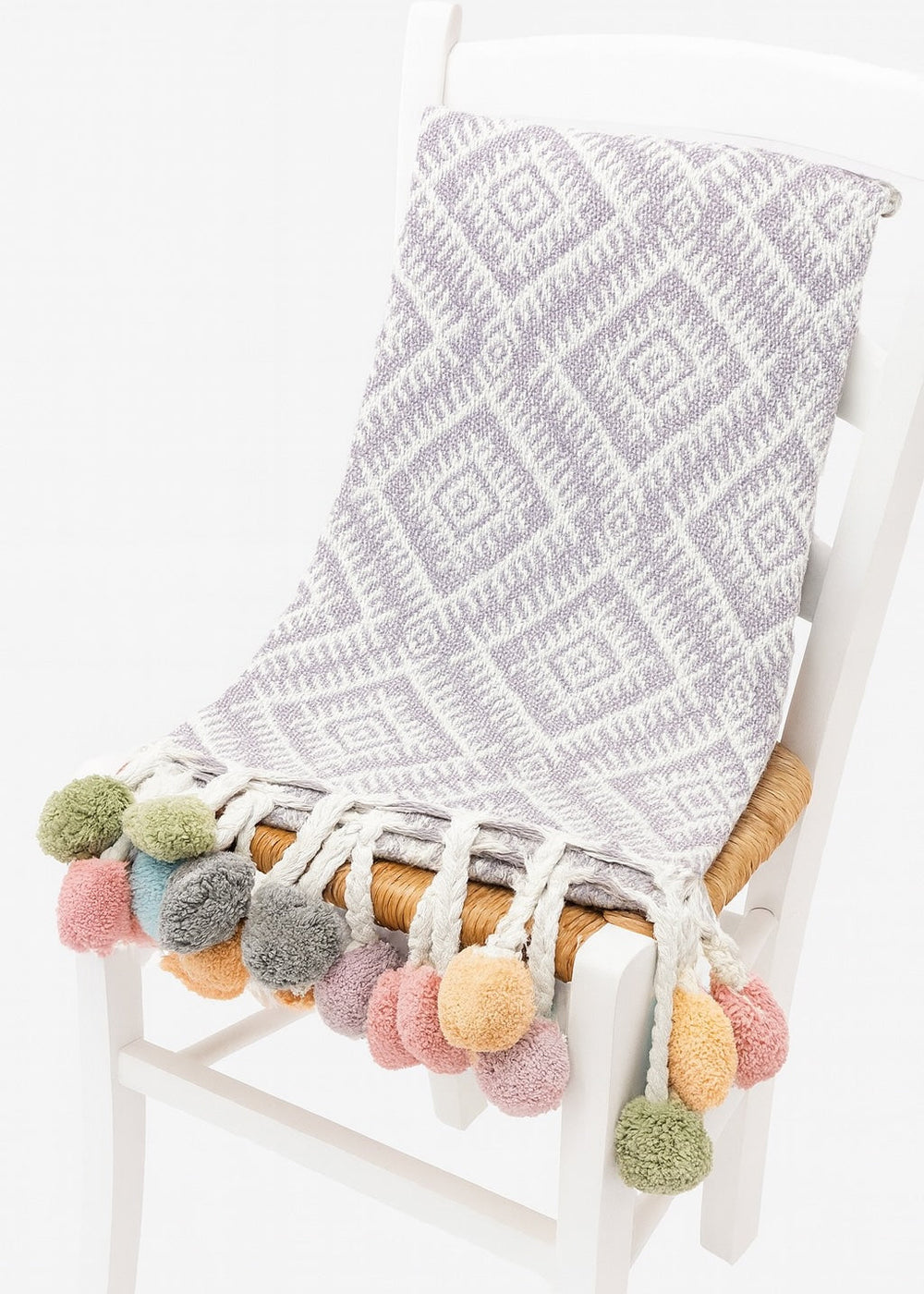 Lilac textured blanket with colourful pom-poms draped over a chair on a white background