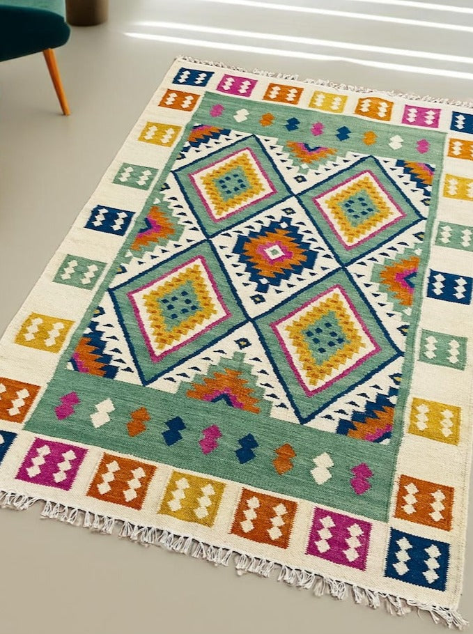 Colourful handwoven Indian kilim rug measuring 120x180 cm, featuring a bold geometric diamond pattern with fringe edges, displayed on a smooth floor.