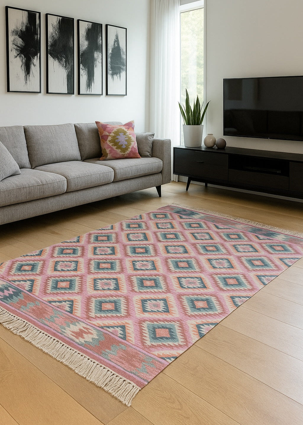 Modern living room with pink and teal geometric rug, grey sofa, wood floor, and abstract wall art.