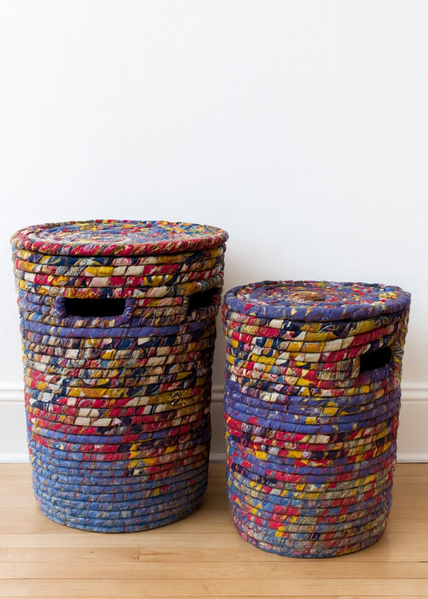 Two colorful woven baskets with lids on a wooden floor.