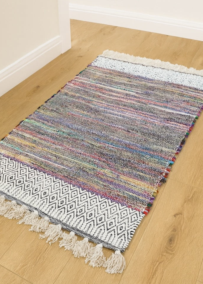 Multicoloured woven rug with tassels on a wooden floor