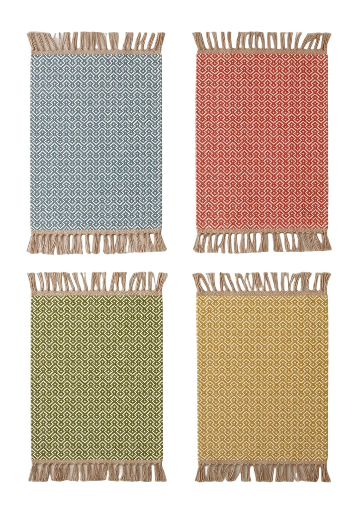 Four rectangular woven rugs with fringe, arranged in a 2x2 grid on a light wood floor. The rugs are in light blue, coral red, sage green, and mustard yellow, each with a geometric pattern.