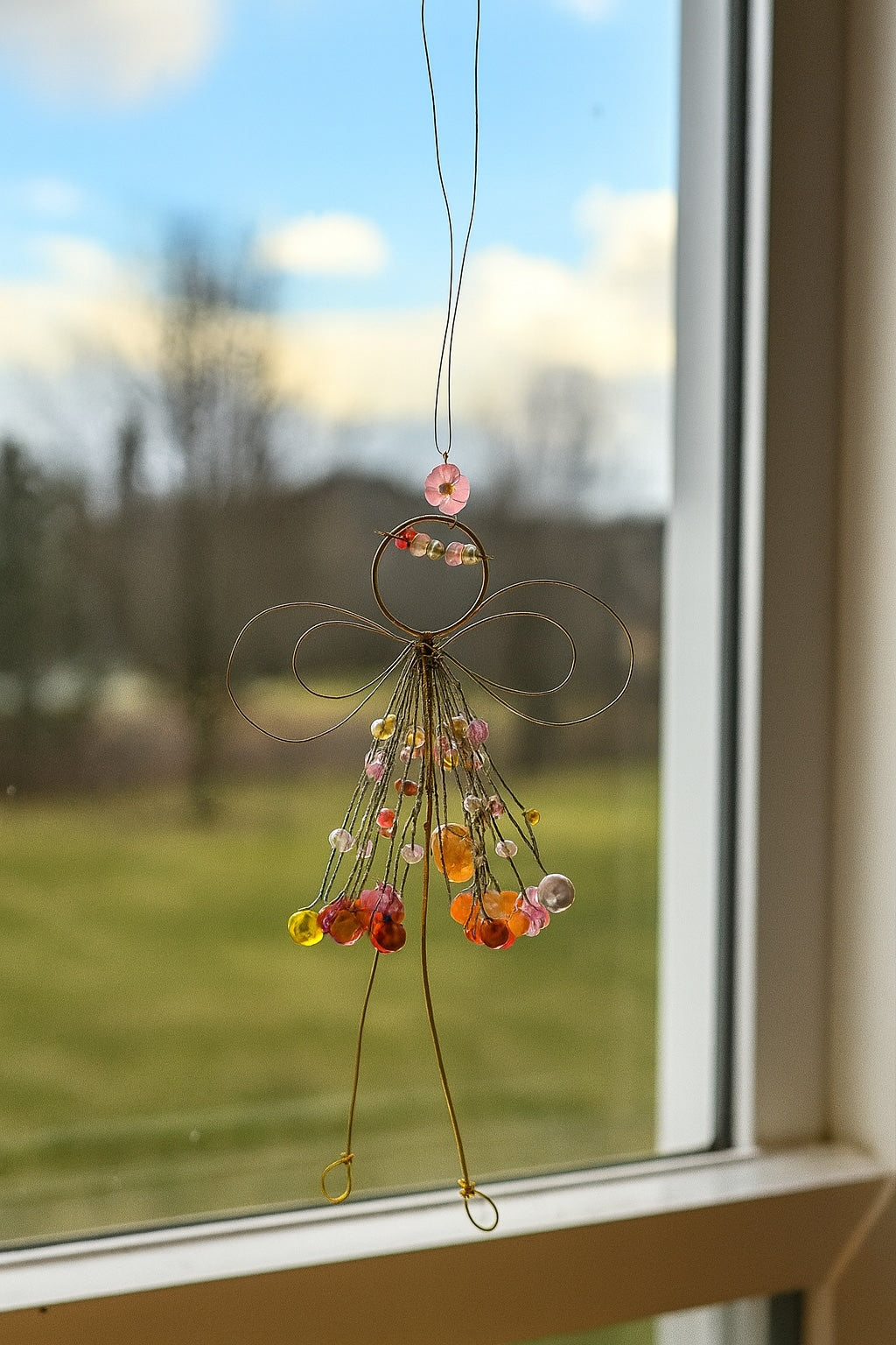 Decorative angel ornament with colourful beads hanging by a window