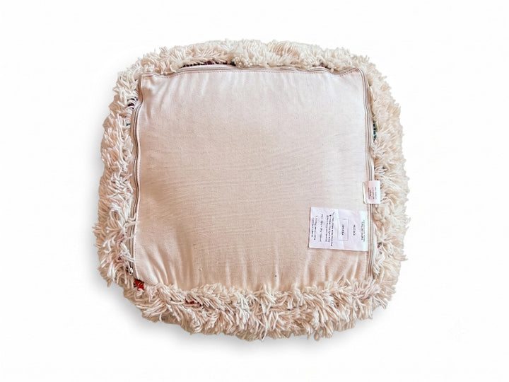 A square floor cushion with a beige satin center and a thick, shaggy cream boucle trim around the border, shown on a white background.