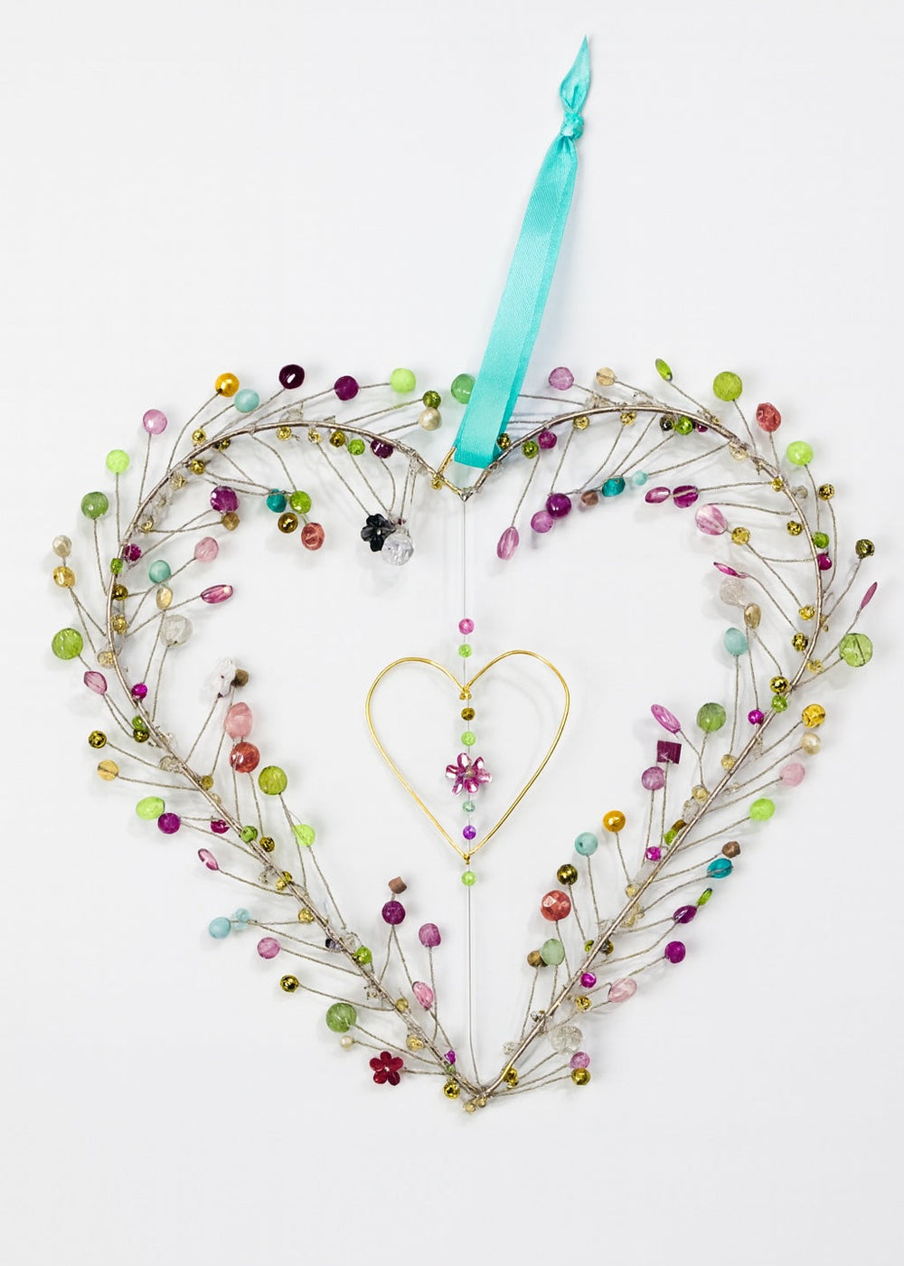Heart-shaped wreath with colourful beads and a blue ribbon on a white background