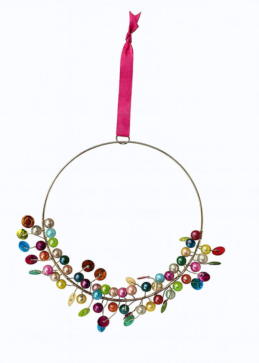 Decorative ring wreath hanging with colourful beads and a pink ribbon on a white background