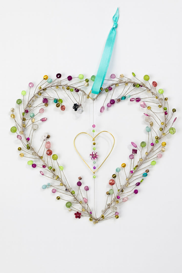Heart-shaped wreath with colourful beads and a teal ribbon on a white background