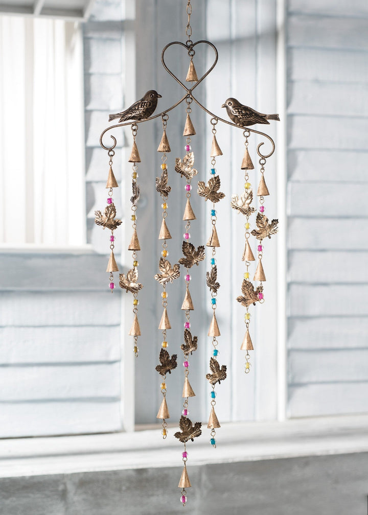 Decorative wind chime with birds and beads hanging in front of a window.