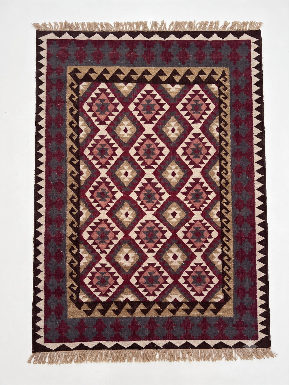 A rectangular woven area rug with a geometric Southwestern-style diamond pattern in burgundy, beige, and dark gray, finished with fringed edges.