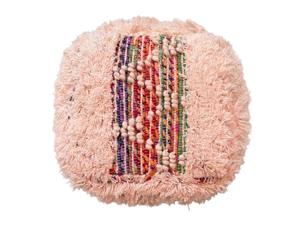A round, fluffy light pink pouf or cushion with a central woven panel featuring vertical stripes of red, green, purple, and orange yarn, accented with rows of small beige beads, shown on a plain white background.