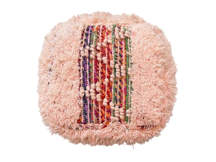 A round, fluffy light pink pouf or cushion with a central woven panel featuring vertical stripes of red, green, purple, and orange yarn, accented with rows of small beige beads, shown on a plain white background.