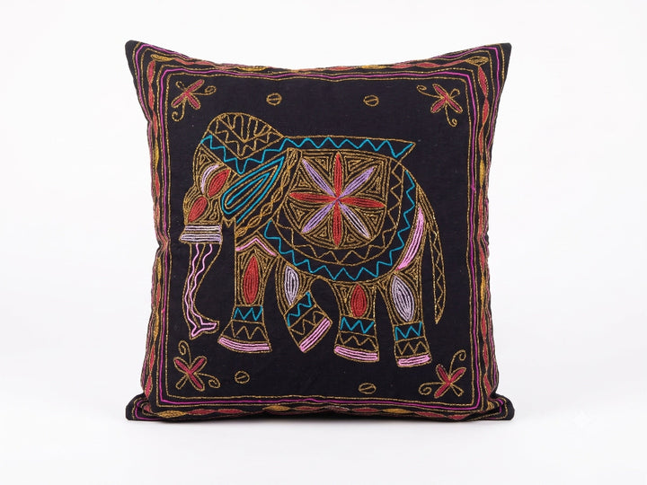 A square black throw pillow featuring a colourful embroidered elephant design in the centre with geometric patterns and a decorative border.