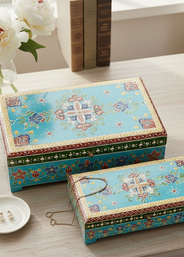 Decorative boxes with floral patterns on a wooden surface with flowers and books in the background.