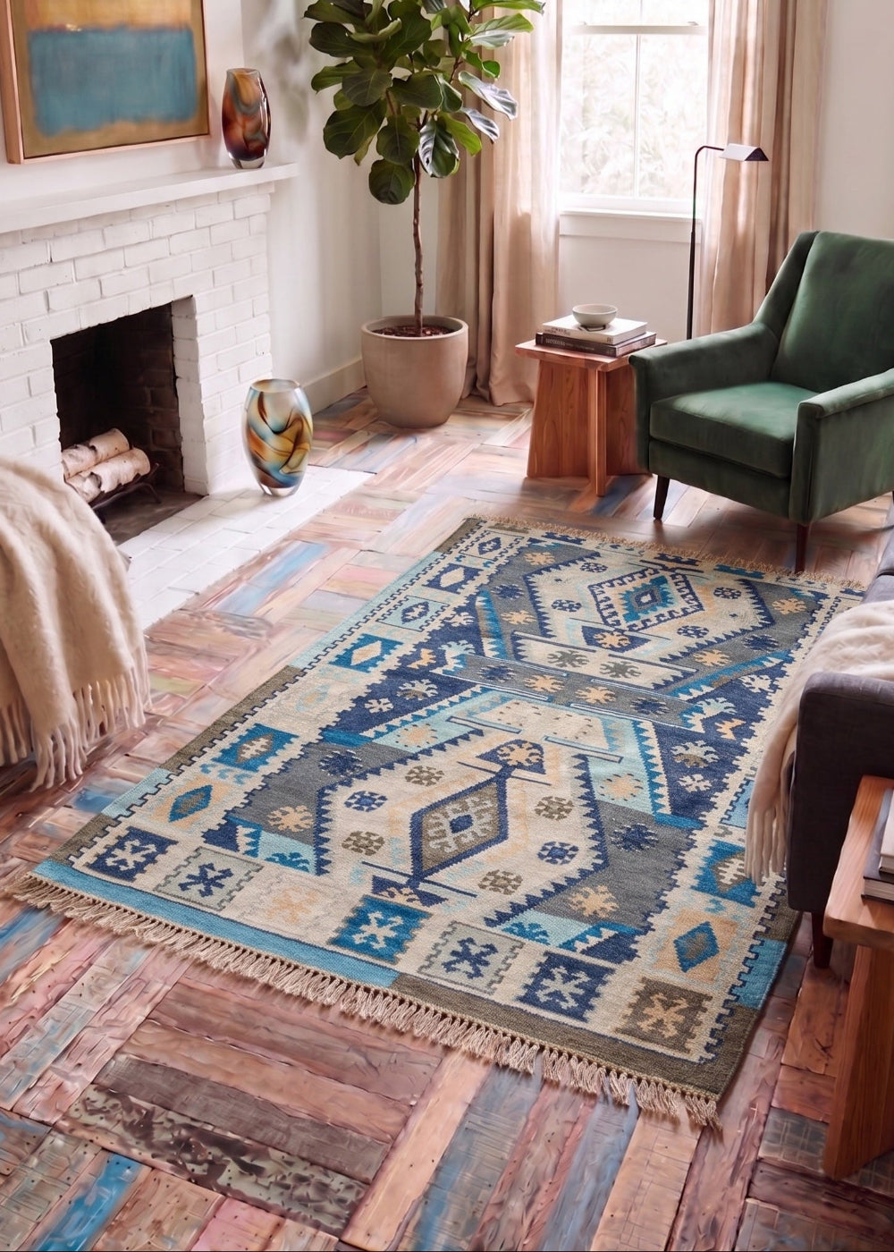 A rectangular area rug with a blue, beige, and grey geometric tribal pattern is displayed on a rustic wood floor in a styled living room with a green armchair, fireplace, and potted plant.