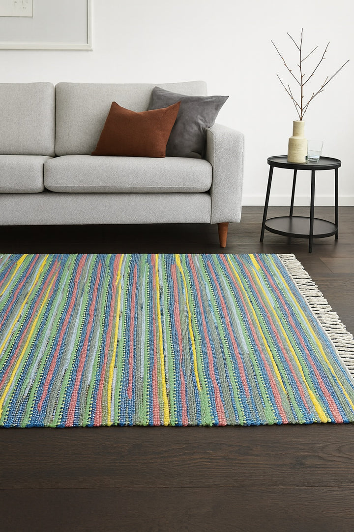 Rag Rug with multi colours on a dark wooden floor and a sofa and table.