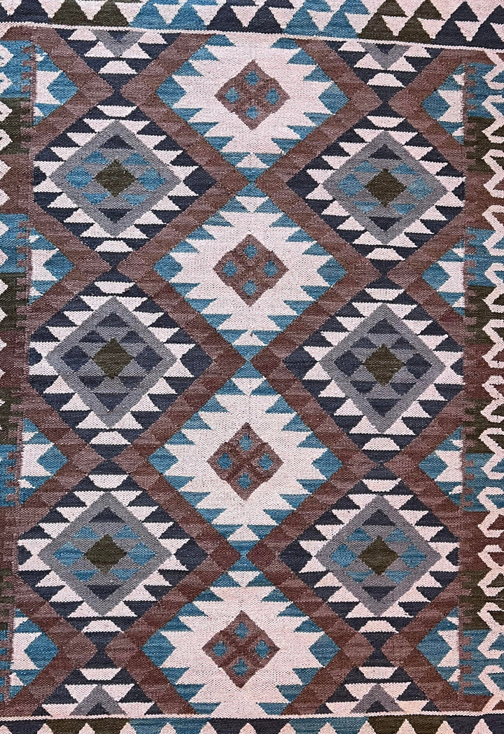 A flat-lay view of a woven kilim rug featuring a geometric diamond pattern in brown, blue, gray, and off-white.