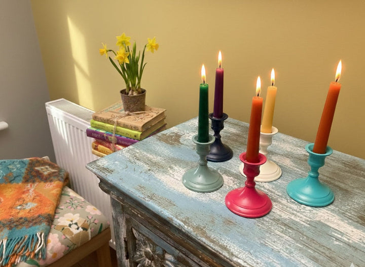 Colourful candles on a rustic table with a plant and books in the background.
