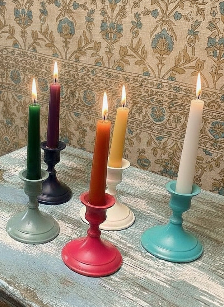 Colourful candles in various holders on a textured surface with patterned wallpaper background