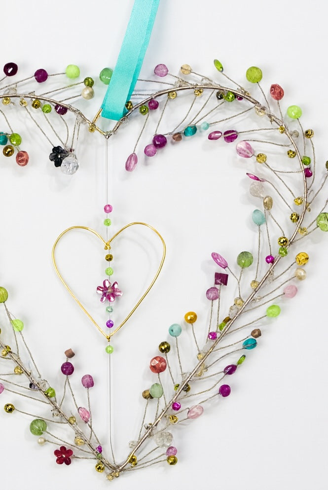 Decorative heart-shaped wreath with colorful beads and a teal ribbon on a white background