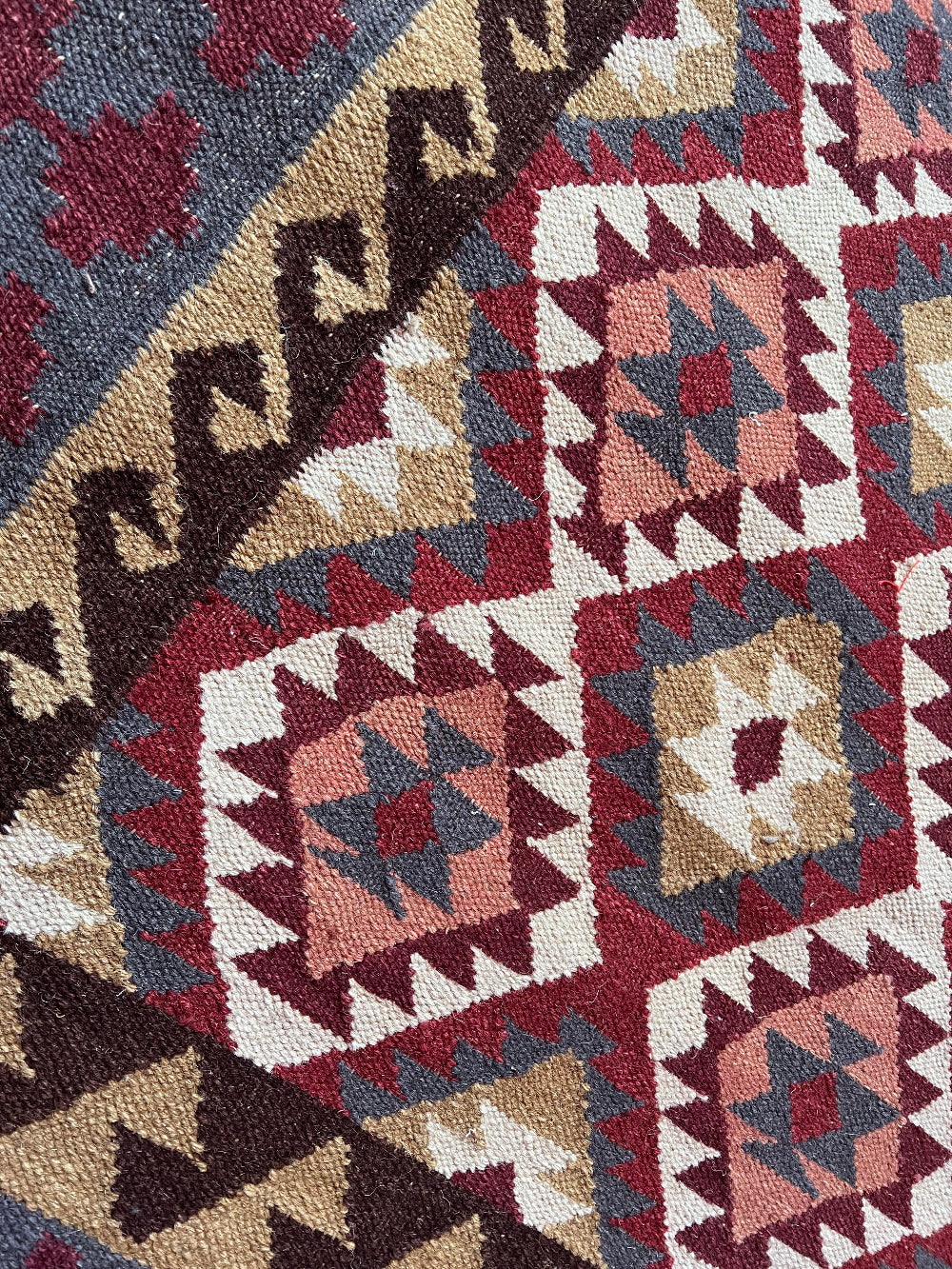 Close-up of a woven textile with a geometric Southwestern-style pattern in burgundy red, beige, brown, and muted blue-gray.