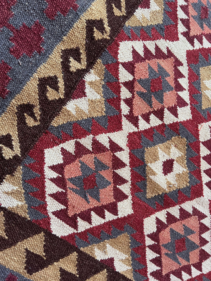 Close-up of a woven textile with a geometric Southwestern-style pattern in burgundy red, beige, brown, and muted blue-gray.