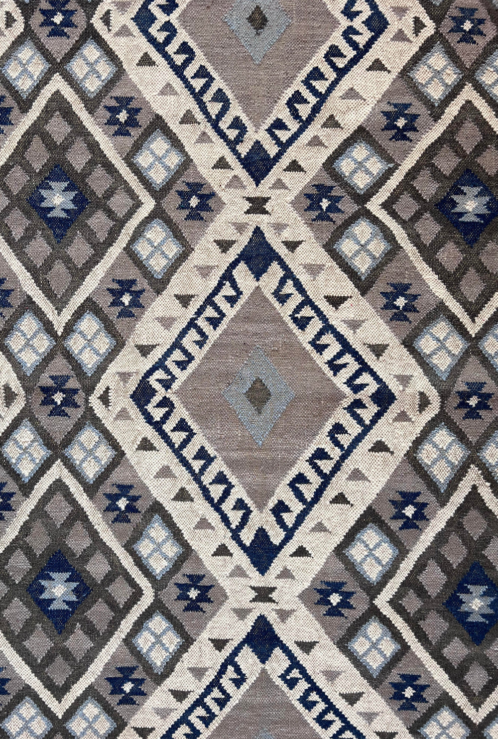 A close-up of a woven rug with a geometric Southwestern-style diamond pattern in navy blue, grey, beige, and off-white.