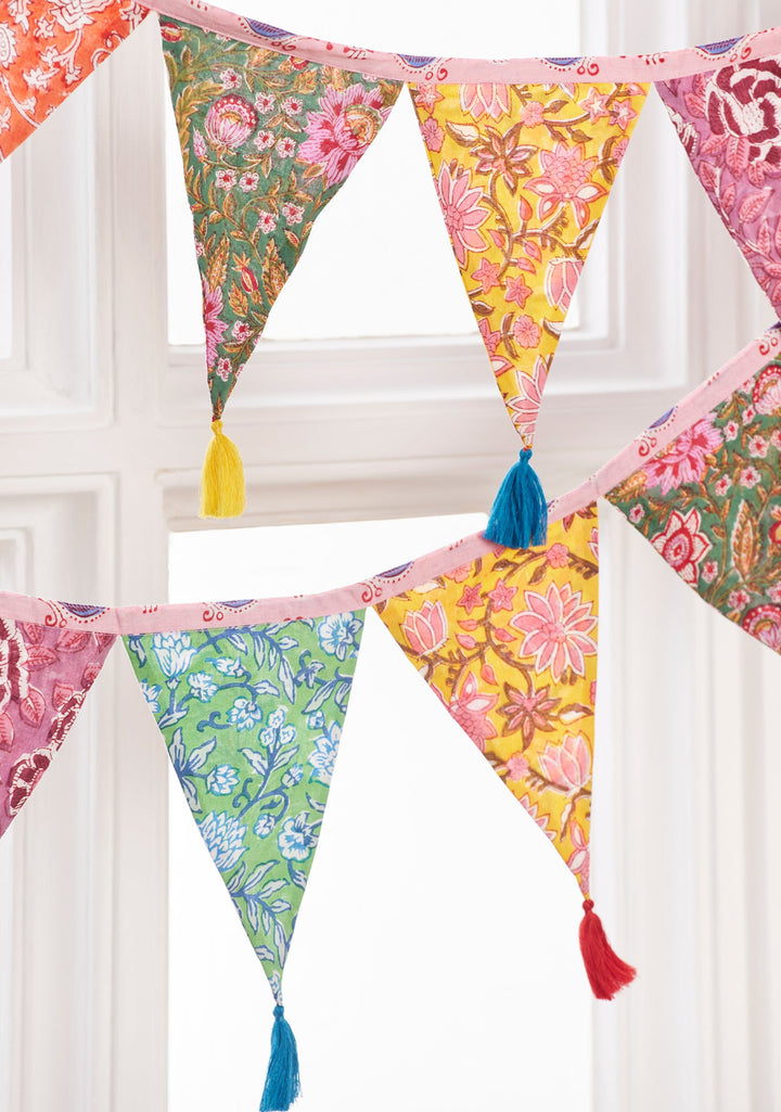 Colourful floral patterned bunting with tassels against a white window frame.