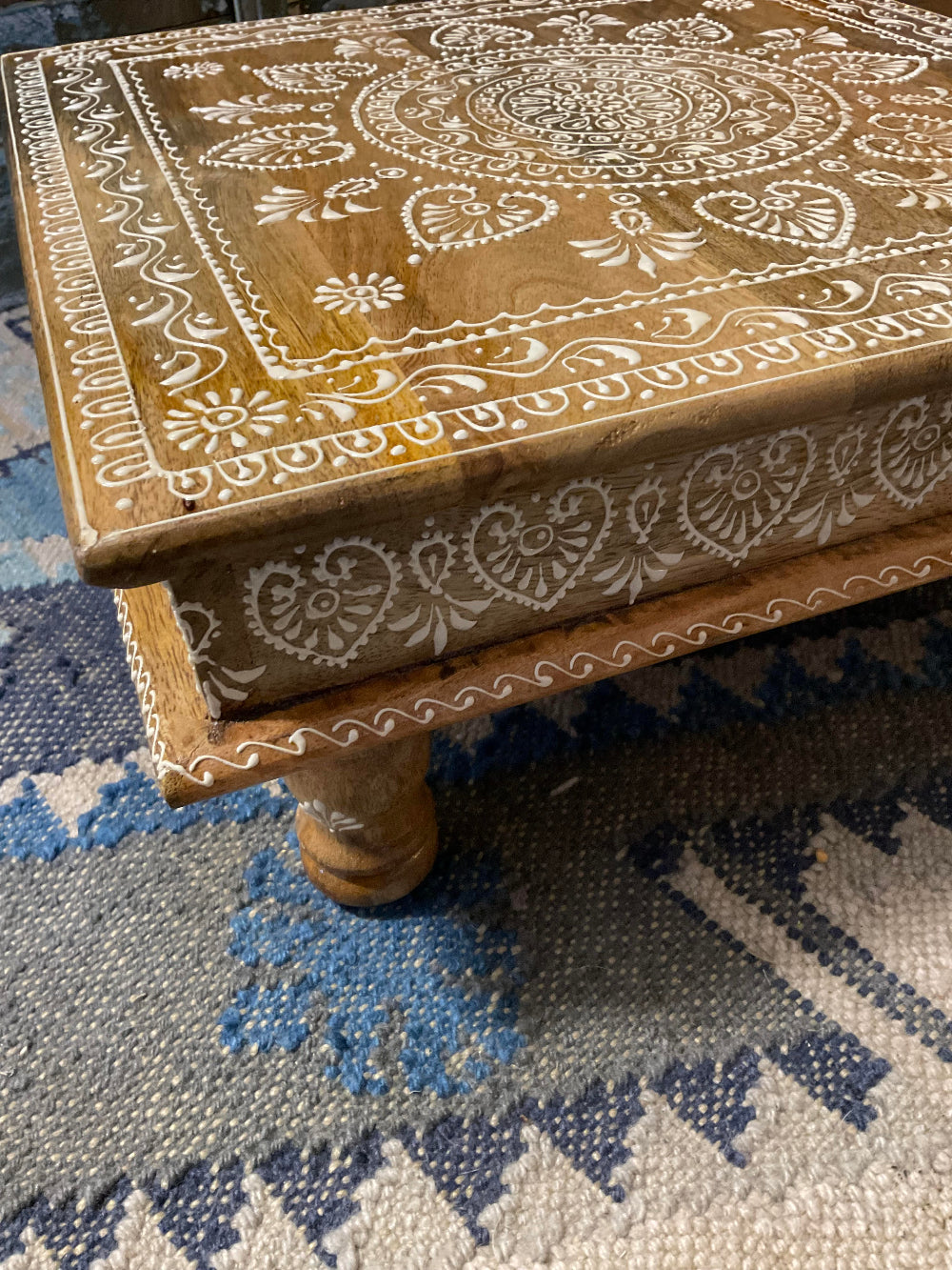 Wooden Bajot Table with intricate white patterns on a blue and white patterned rug