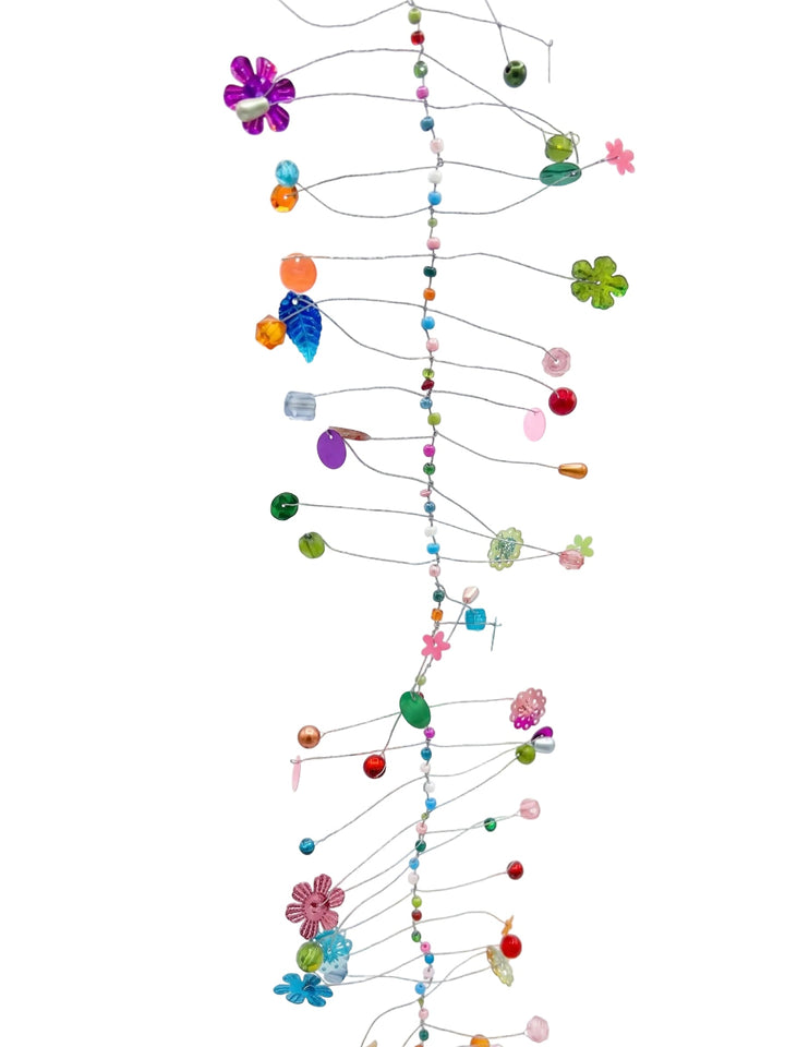A colourful mobile hanging from thin metal wires, decorated with small beads, flowers, leaves, and geometric shapes in vibrant shades of green, blue, pink, purple, orange, and red against a plain white background.