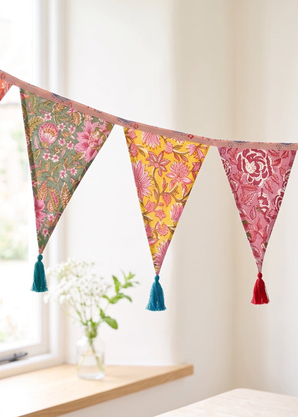 Colourful floral bunting with tassels hanging against a white wall.