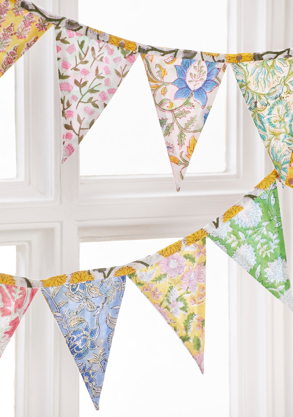 Colourful floral fabric bunting hanging against a white window frame.