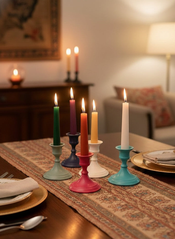 Colourful candles in various candlestick holders on a dining table with a warm ambiance.