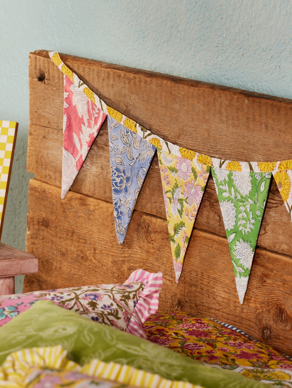 Colourful fabric bunting on a wooden headboard with pillows underneath.
