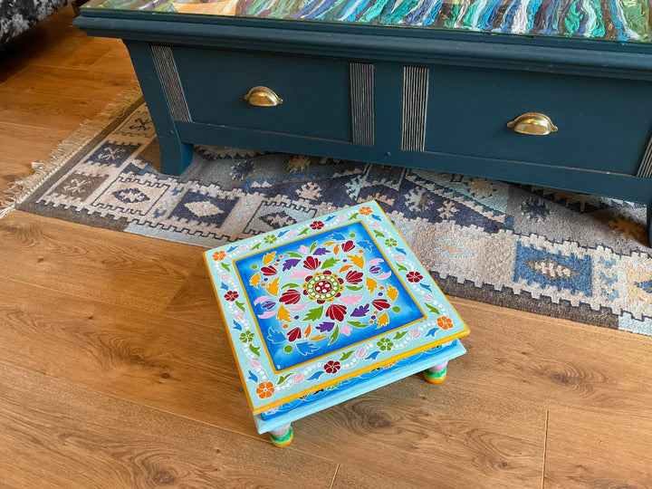 Decorative small table with floral patterns on a wooden floor in front of a blue chest of drawers