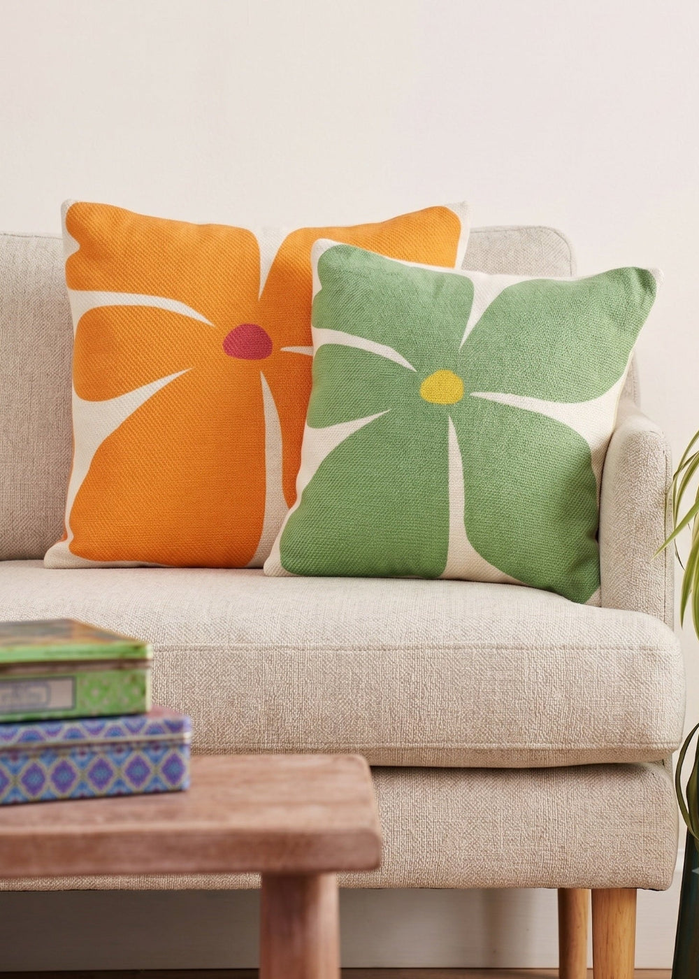 Screen-printed bold flower cushion cover in meadow green and vibrant orange on a beige fabric sofa.