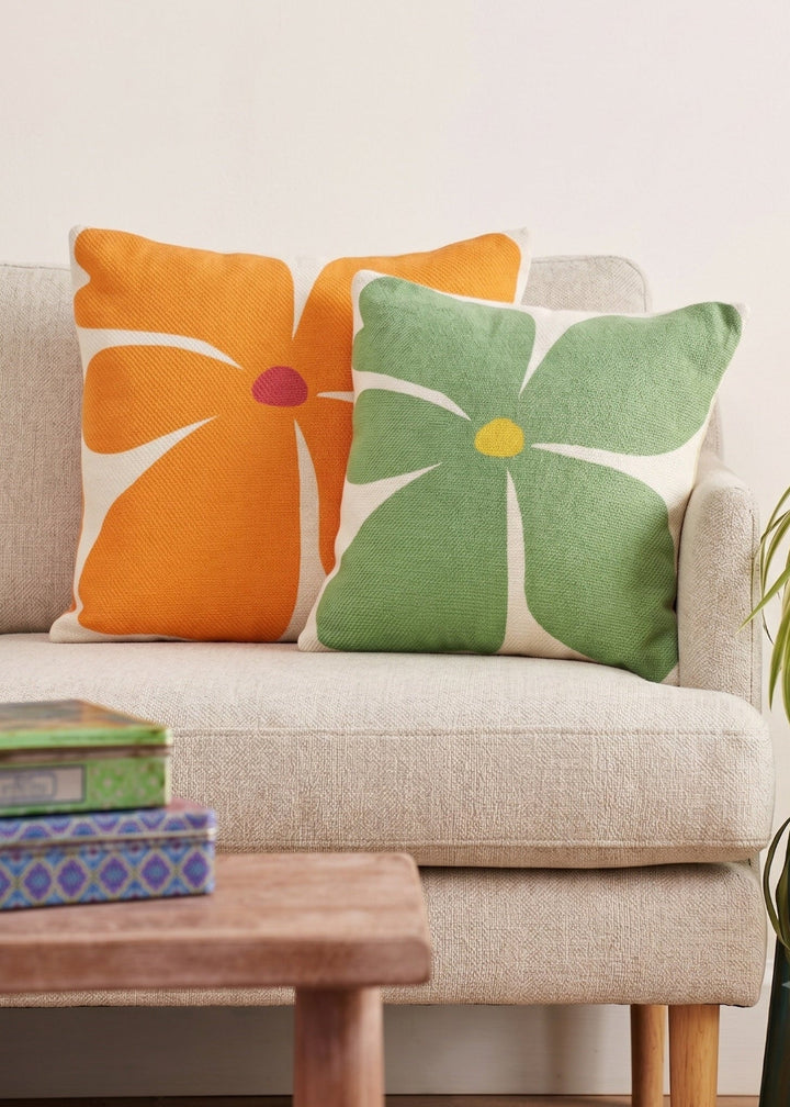 Screen-printed bold flower cushion cover in meadow green and vibrant orange on a beige fabric sofa.
