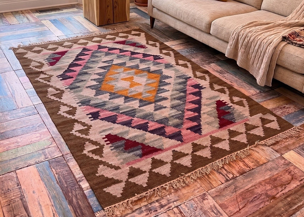 A rectangular area rug with a Southwestern geometric pattern in brown, beige, yellow, pink, and blue, styled on a rustic wood floor in a cosy living room next to a beige sofa.