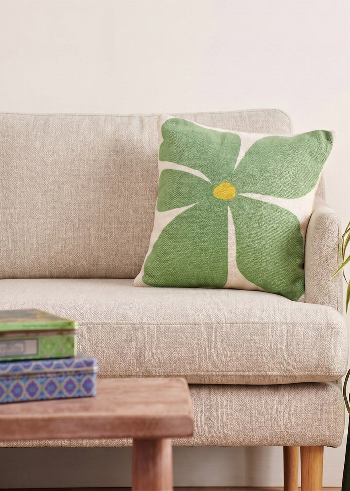 Green floral pillow on a beige sofa with a wooden coffee table and plant in the background.