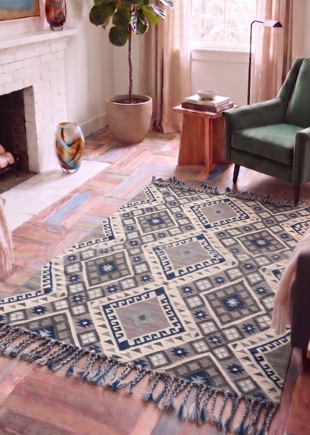 A rectangular area rug with a geometric Southwestern-style pattern in beige, navy, and grey, styled on a rustic wood floor in a cozy living room with a fireplace, green armchair, and potted plant.