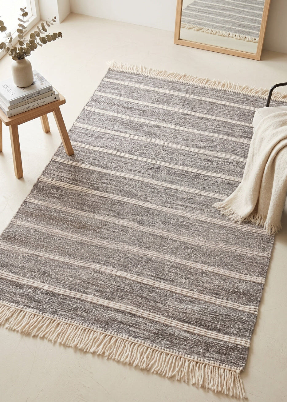 Striped area rug with tassels on a light-coloured floor, with a small table and decorative items in the background.