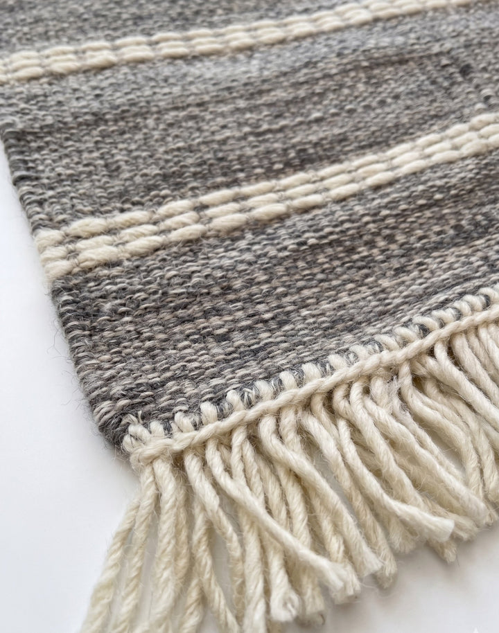Grey and white striped rug with fringes on a white background