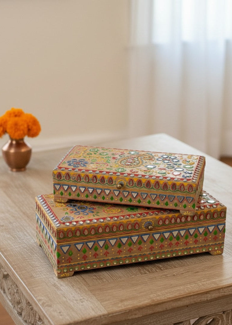 Two decorative boxes with intricate patterns stacked on a wooden table.