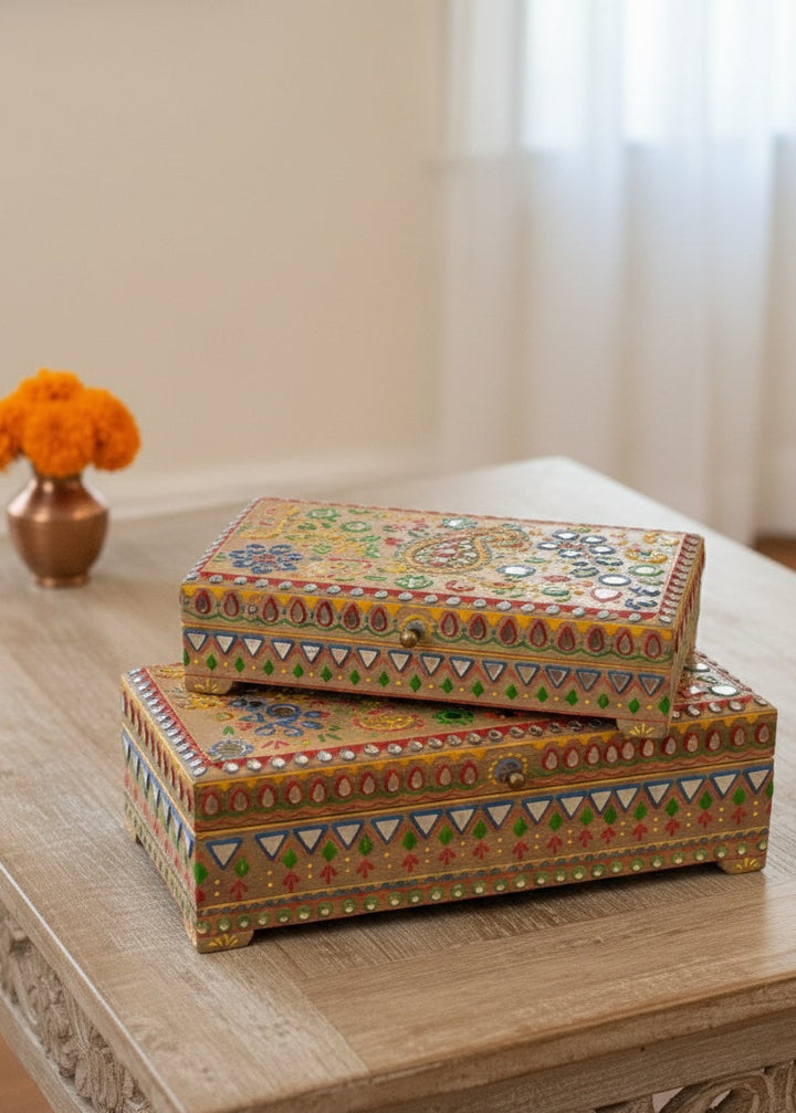 Two decorative boxes with intricate patterns stacked on a wooden table.